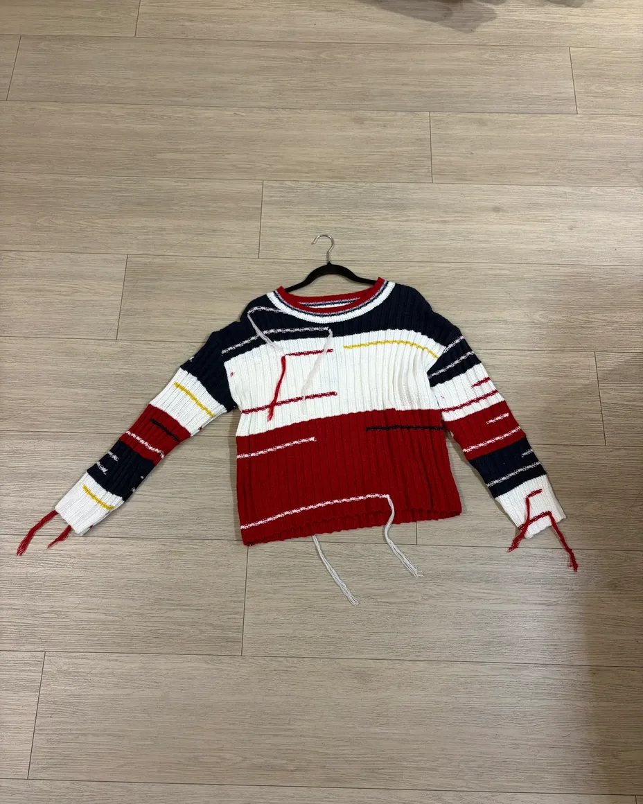 Suéter tejido a rayas rojo, azul y blanco en un gancho sobre el piso de la tienda — foto original